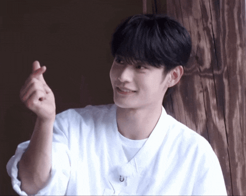 a young man wearing a white shirt is making a heart shape with his hands