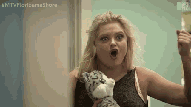 a woman is holding a stuffed animal in her hands and making a surprised face .