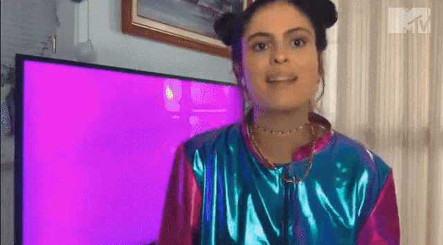 a woman in a blue and pink jacket is standing in front of a purple television .