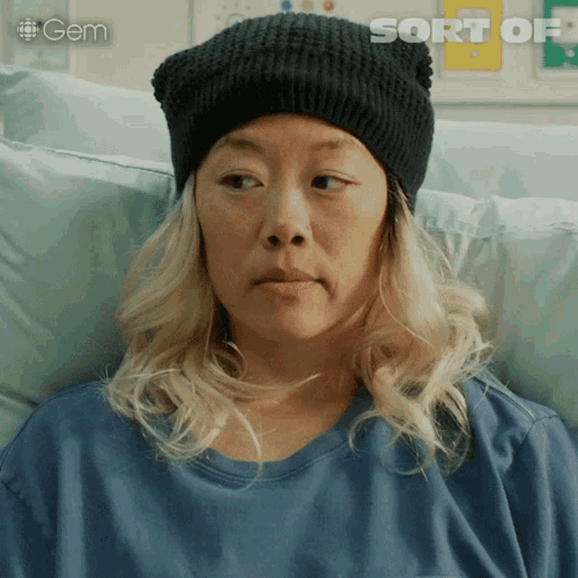 a woman in a hospital bed is wearing a black hat and a blue shirt that says gem