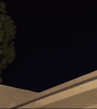 a person is jumping off a building at night with a tree in the background