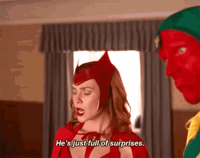 a woman in a red cape is standing next to a man in a red hat and talking .