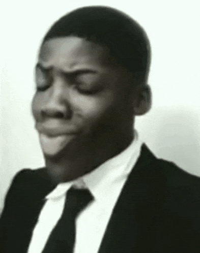 a black and white photo of a man wearing a suit and tie making a funny face .