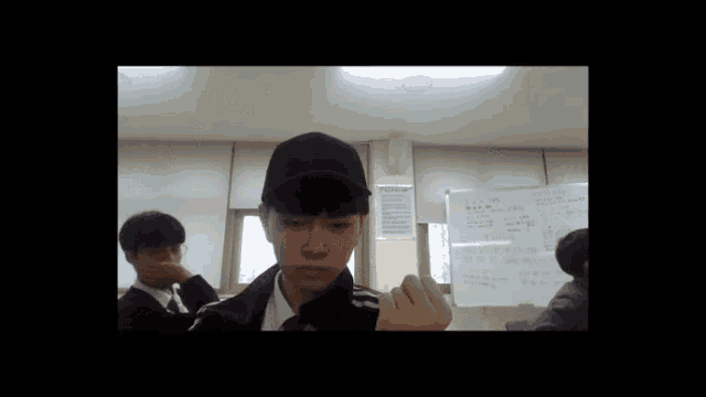 a young man wearing a black hat stands in front of a white board