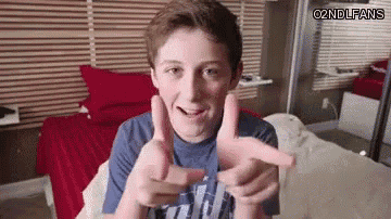 a young boy is making a gun sign with his hands while sitting on a bed in a bedroom .