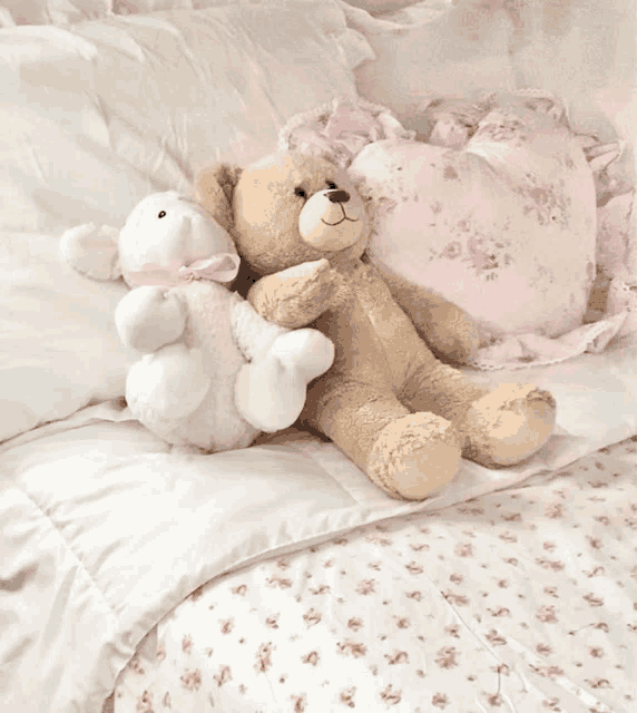 two teddy bears are laying on a bed with a pink pillow