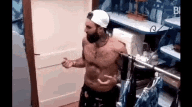 a shirtless man with a beard and a hat is standing in a room .