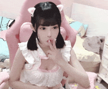a girl with pigtails and cat ears is sitting in a pink chair with her finger to her mouth