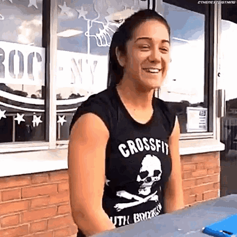 a woman wearing a crossfit shirt is smiling and sitting at a table .