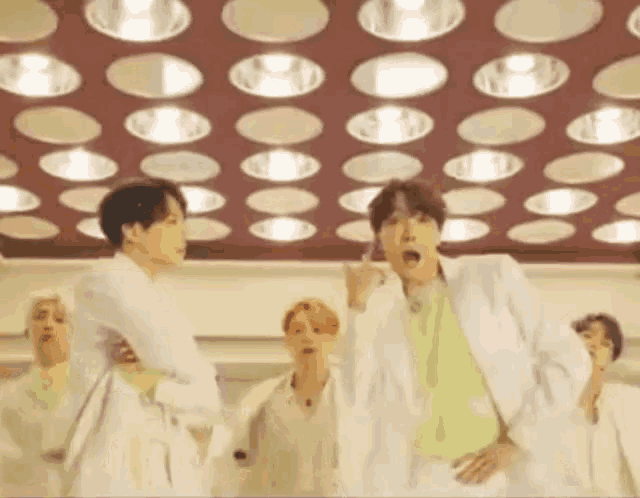 a group of men in white suits are dancing in front of a ceiling with circles of lights .