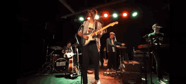 a man playing a guitar on a stage with a drum set that says blank on it
