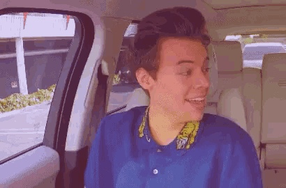 a man in a blue shirt is sitting in the back seat of a car .