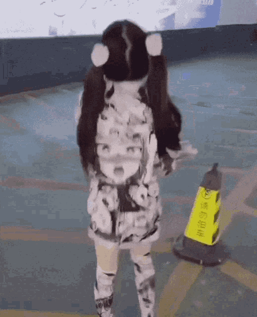 a girl with pigtails is standing next to a yellow cone that has chinese writing on it