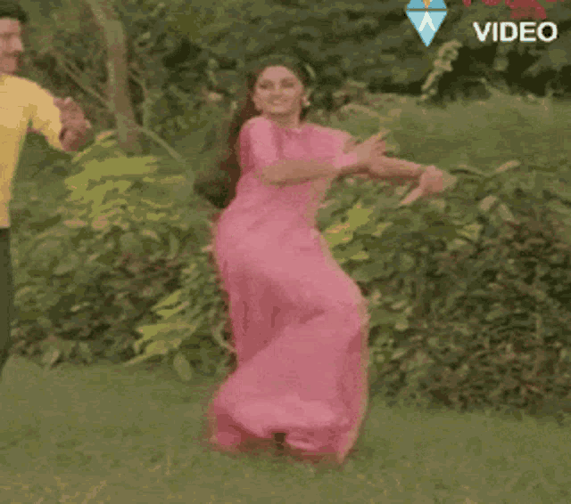 a woman in a pink saree is dancing in the grass with a man .