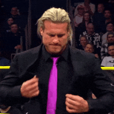 a man wearing a black suit and a purple tie with a crowd behind him