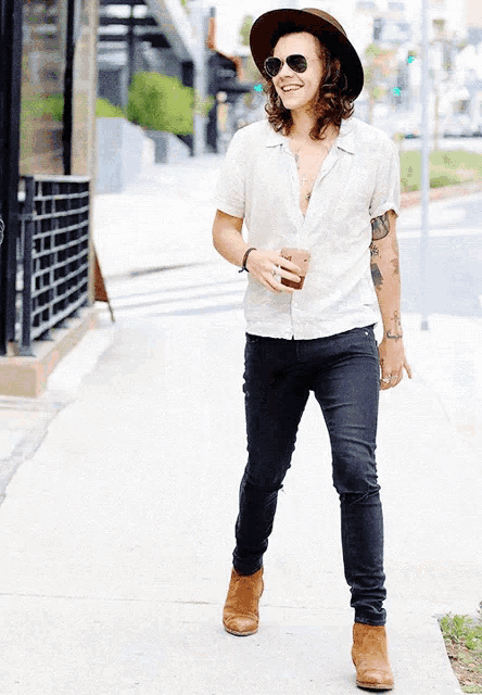 a man wearing a hat and sunglasses walks down a sidewalk