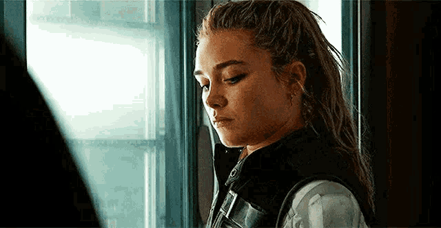 a woman is standing in front of a window and looking out .