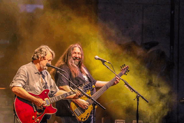 two men are playing guitars and singing into microphones on stage