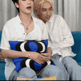 two people are sitting on a blue couch and one has a blue pillow with a black and white letter o on it