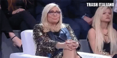 a woman in a sequined jacket is sitting in a chair with her legs crossed and making a funny face .