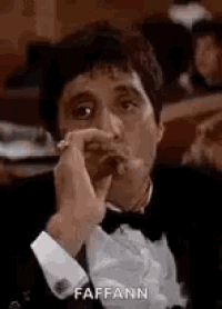 a man in a tuxedo is smoking a cigar in a room .