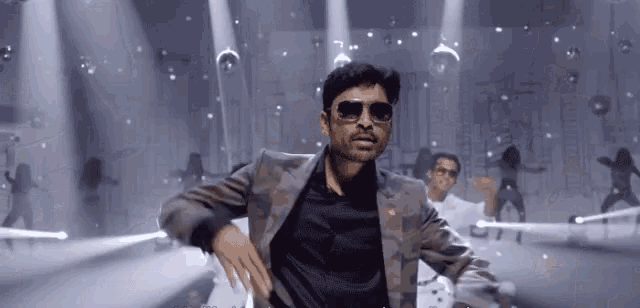 a man in a suit and sunglasses is dancing in front of a crowd .