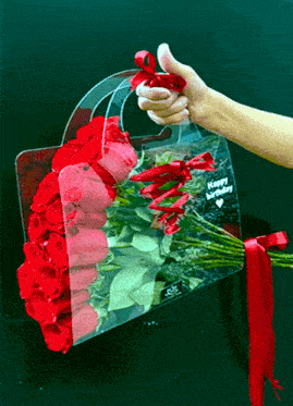 a person is holding a clear bag of red roses that says happy birthday on it