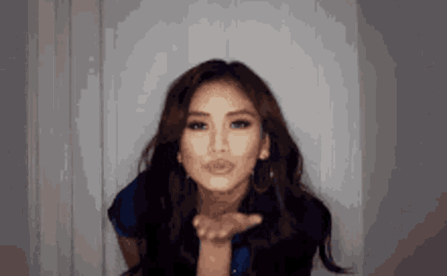 a woman is blowing a kiss at the camera while wearing a blue shirt .