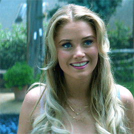 a woman with blonde hair is smiling and wearing a white tank top