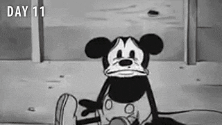 a black and white cartoon of mickey mouse sitting on the ground with a sad face .