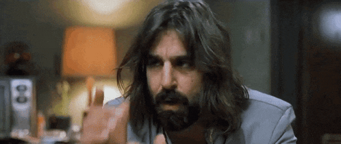 a man with long hair and a beard is giving the middle finger while wearing a suit .