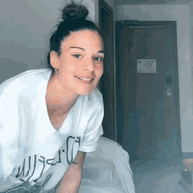 a woman wearing a white t-shirt that says ' a ' on it is smiling