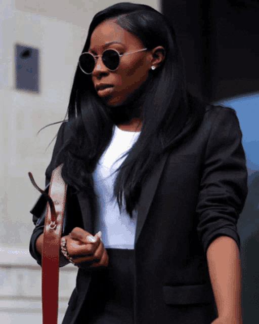 a woman wearing sunglasses and a black jacket holds a red strap