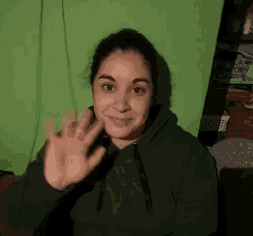 a woman in a green hoodie waves her hand in front of a green wall