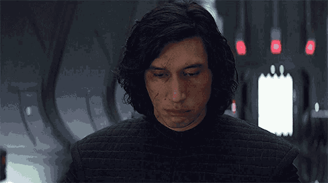 a man with long hair is wearing a black jacket and looking at the camera .