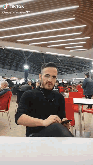 a man is sitting at a table in a food court with a tiktok watermark on the bottom right