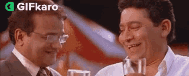 two men are sitting next to each other holding glasses of water and smiling .
