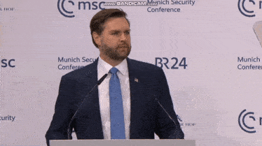 a man in a suit and tie stands at a podium in front of a wall that says munich security conference