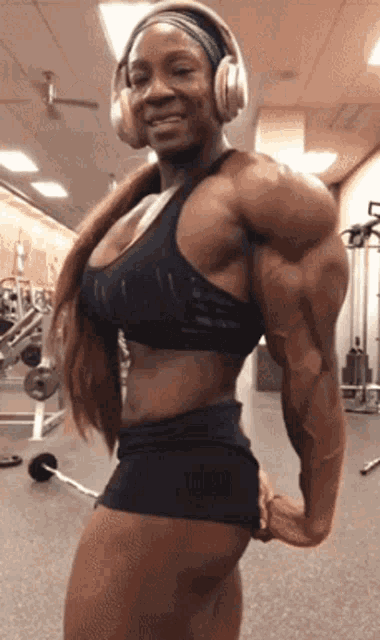 a very muscular woman wearing headphones is standing in a gym .