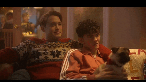 two young men are sitting on a couch looking at their cell phones