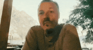 a man with a beard is sitting at a table with a mountain in the background