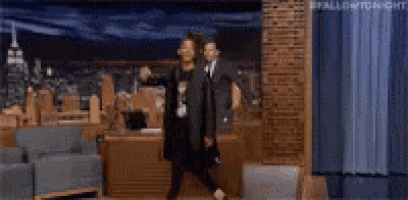 a man in a suit is standing in front of a couch in a room with a city in the background .