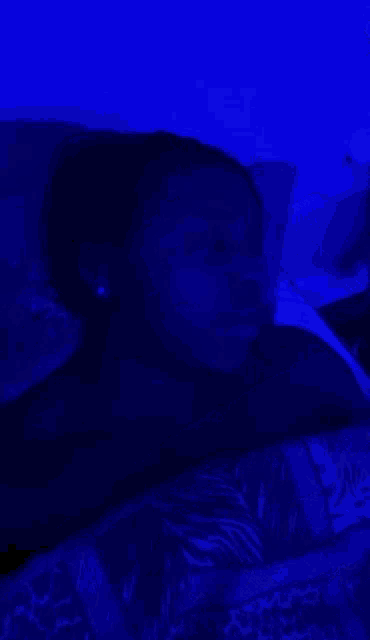 a woman is laying in bed under a blue light and looking at the camera .