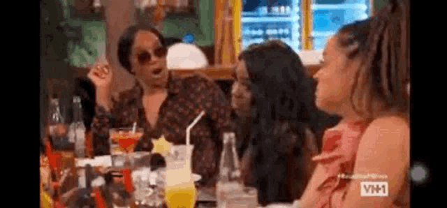 a group of women are sitting at a table with drinks and talking .