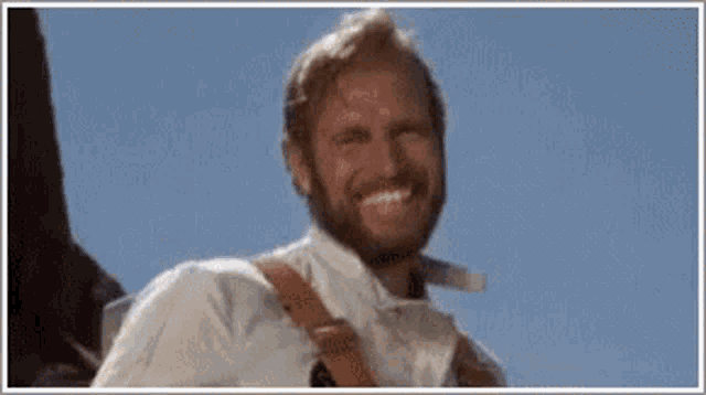 a man with a beard and a white shirt is smiling in front of a blue sky .