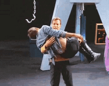 a man is holding another man in his arms in a dark room