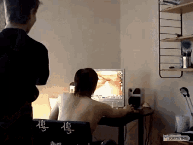 a man sitting in front of a computer with chinese characters on the back of his chair