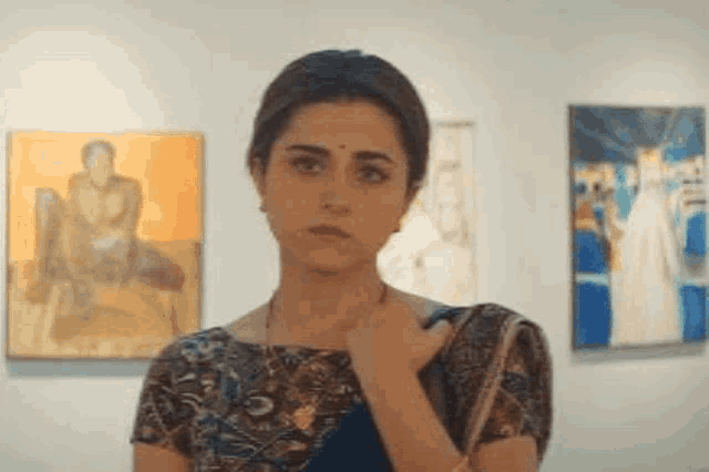 a woman in a saree is standing in front of a wall with paintings on it .