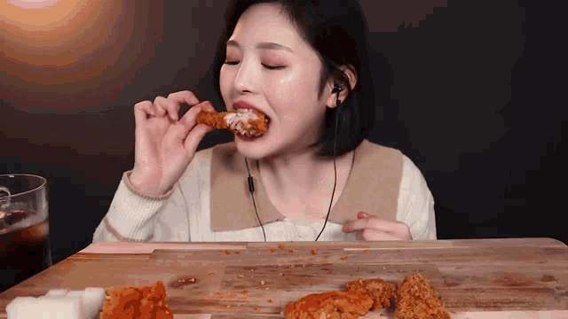 a woman is sitting at a table eating a piece of fried chicken .