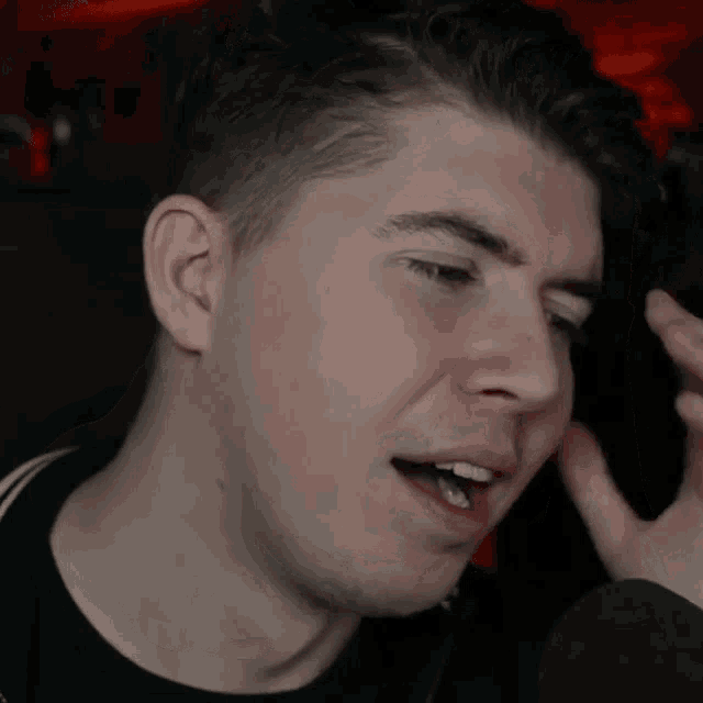 a close up of a man covering his face with his hand while talking into a microphone